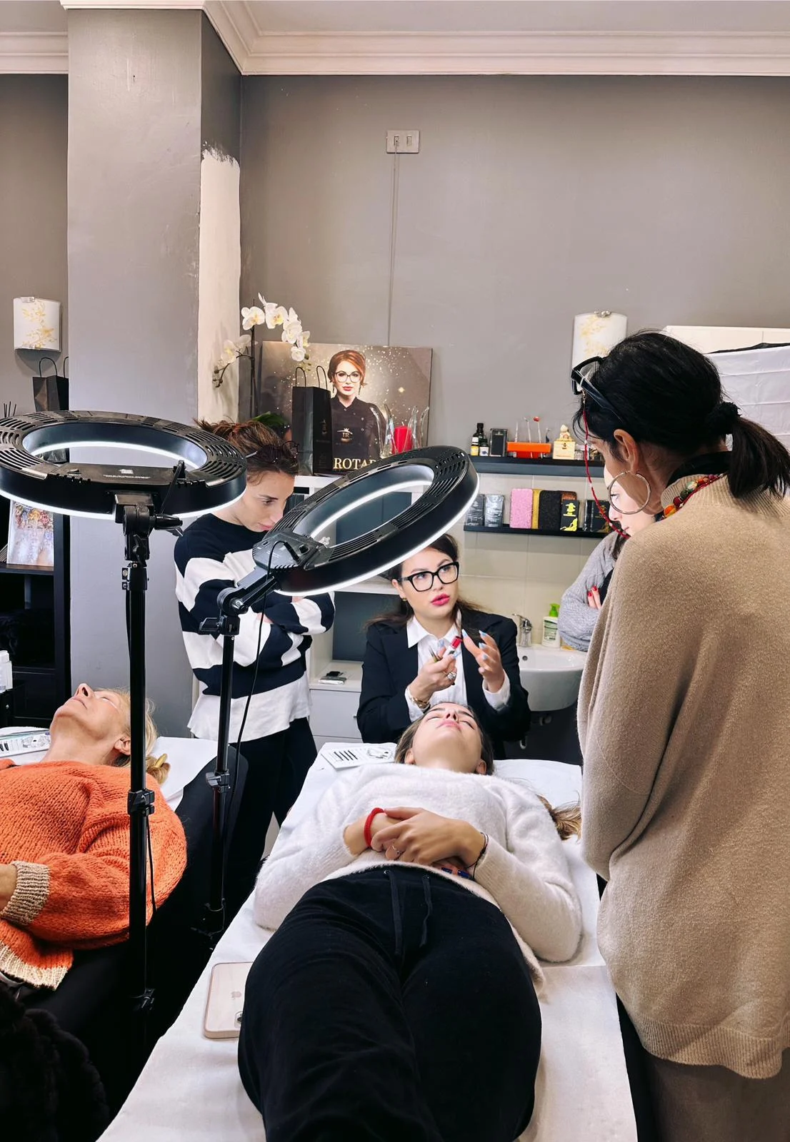Lezione di estetica con estetisti e clienti, attrezzature professionali e ambiente di lavoro accogliente.